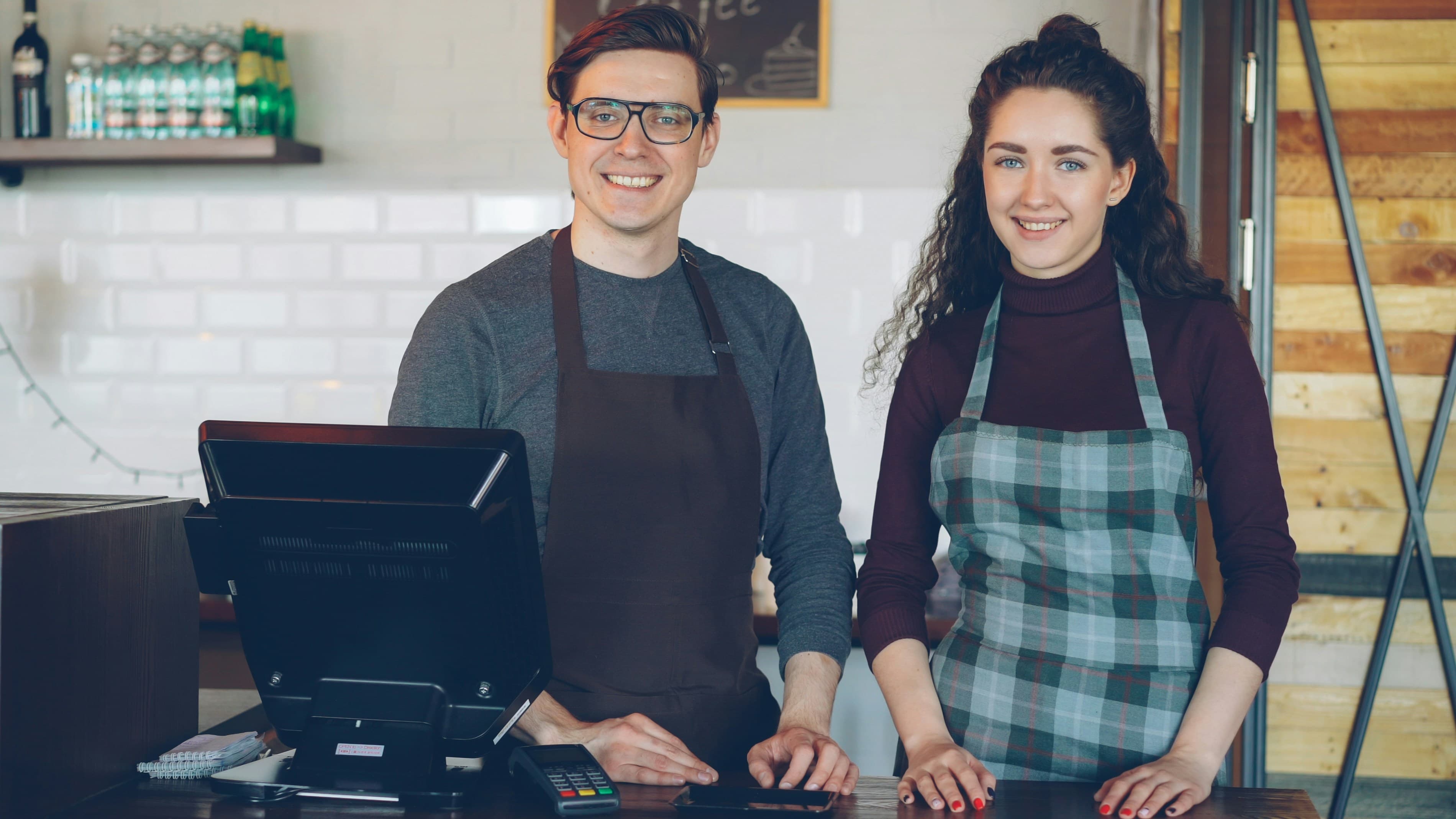 Two smiling cafe workers standing behind a counter